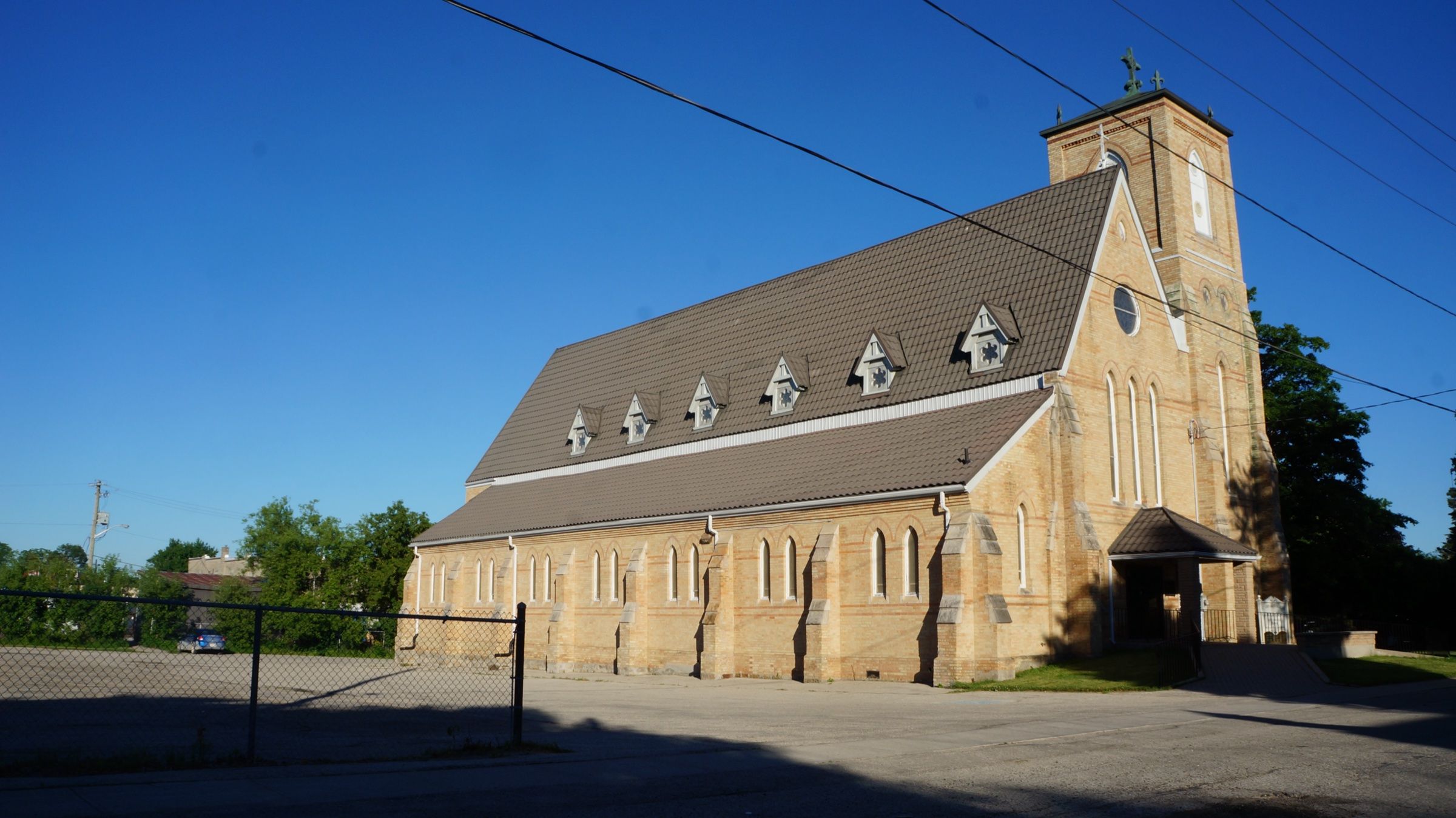 St. John the Evangelist Catholic Church, a long buff-brick church with dormer windows along the nave roof and a square bell tower topped by a cross